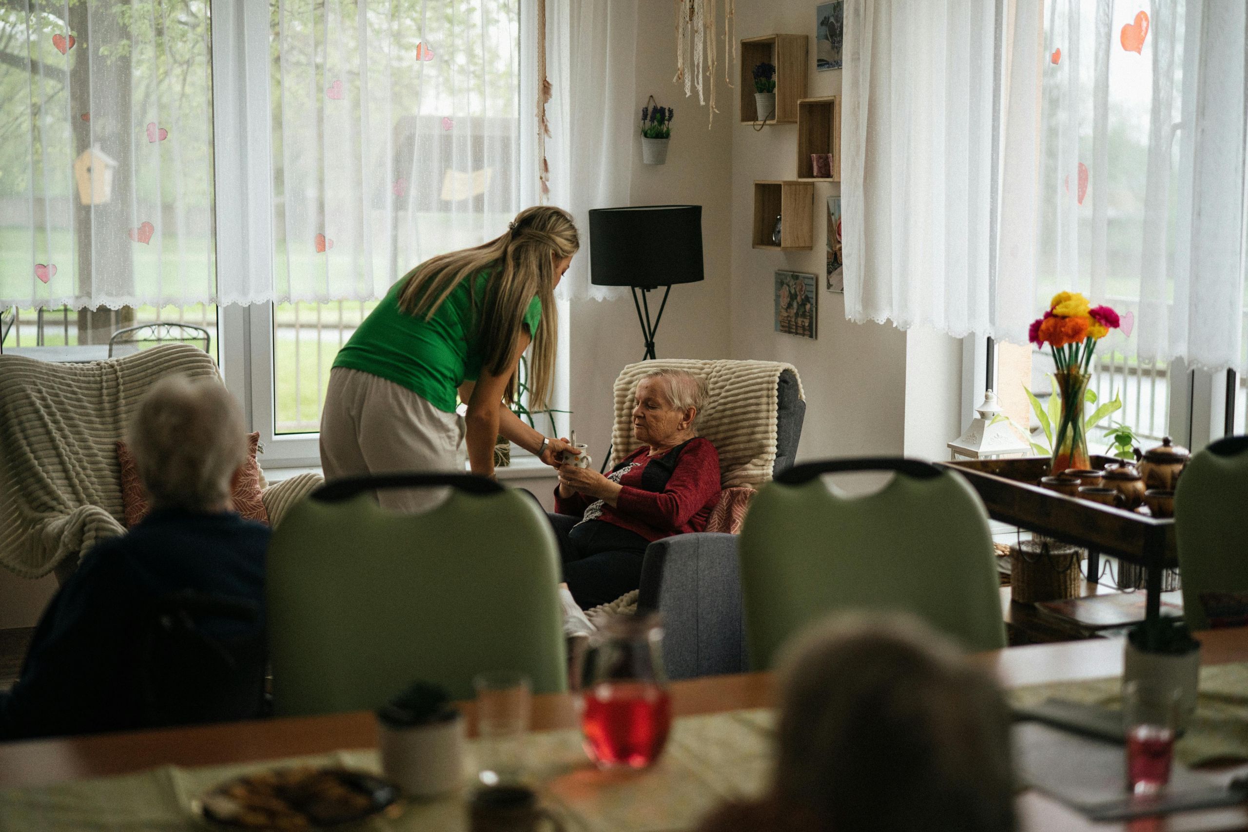 Caregivers A caregiver in a green shirt assisting a senior woman in a comfortable living room setting, illustrating ADRC caregiver support services.