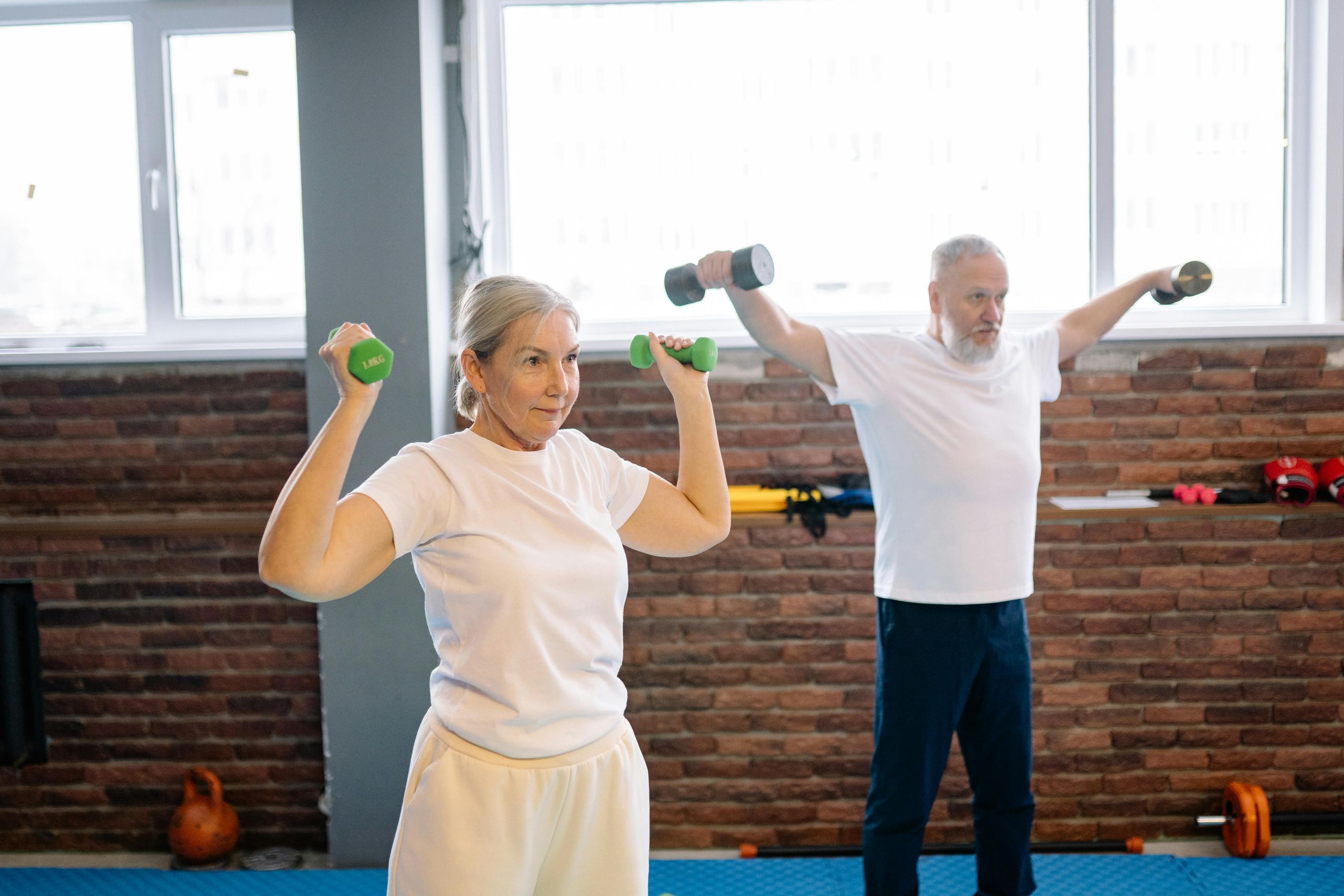 Health Wellness and Safety A senior man and woman exercising with dumbbells in a fitness class, promoting active aging and wellness for Waupaca County seniors.